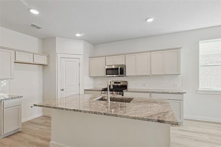 Kitchen featuring light hardwood / wood-style floors, stainless steel appliances, light stone counters, and a kitchen island with sink