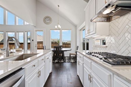 Kitchen with tasteful backsplash, white cabinetry, light stone countertops, appliances with stainless steel finishes, and pendant lighting