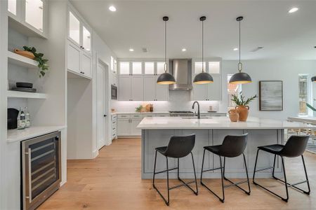 Kitchen with wall chimney range hood, light hardwood / wood-style flooring, beverage cooler, a wealth of natural light, and white cabinets