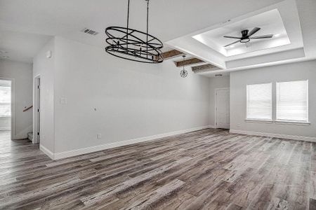 Empty room featuring hardwood / wood-style flooring, ceiling fan with notable chandelier, and a tray ceiling