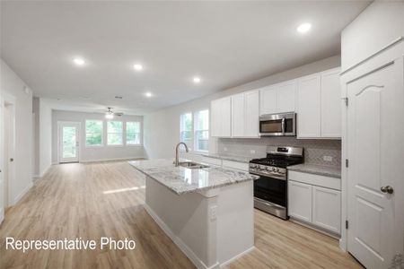 Kitchen with ceiling fan, light wood-type flooring, an island with sink, white cabinetry, and stainless steel appliances