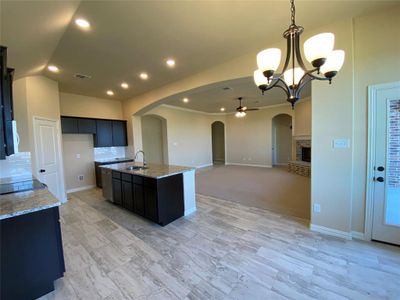 Kitchen featuring light stone counters, an island with sink, sink, decorative light fixtures, and ceiling fan with notable chandelier