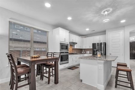 Kitchen with a center island with sink, white cabinets, appliances with stainless steel finishes, light stone counters, and under cabinet range hood