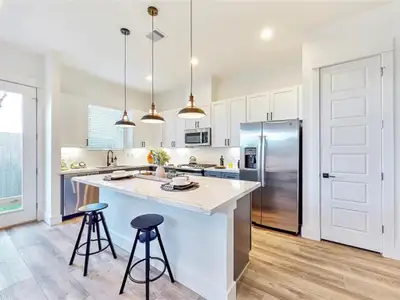 The kitchen is bright and airy, with large windows that let in plenty of natural light. The room is decorated with a few plants and other decorative items, creating a warm and inviting atmosphere. The kitchen is well-equipped, with a microwave, oven, and dishwasher. The overall design of the kitchen is modern and minimalist, with a focus on functionality and clean lines.