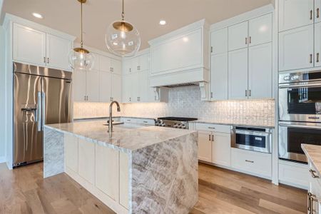 Kitchen with light wood-type flooring, light stone counters, hanging light fixtures, appliances with stainless steel finishes, and white cabinets