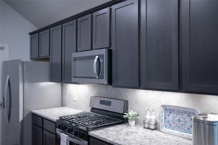 Kitchen with backsplash, stainless steel appliances, and light stone counters