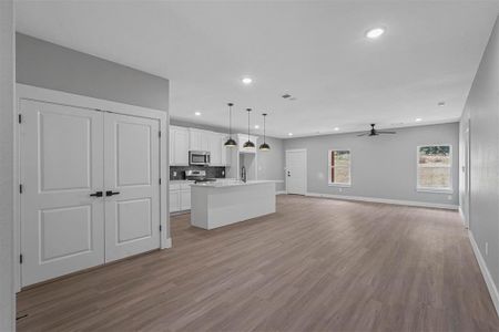 Kitchen featuring stainless steel appliances, hanging light fixtures, a center island with sink, white cabinets, and light hardwood / wood-style floors