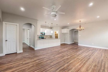 Large living room with ceiling fan with notable chandelier, sink, and wood-type flooring