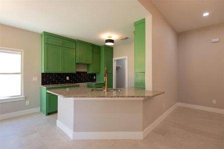 Kitchen featuring light stone countertops, kitchen peninsula, green cabinets, and backsplash