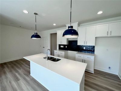 Kitchen featuring hanging light fixtures, a kitchen island with sink, sink, and dark wood-type flooring