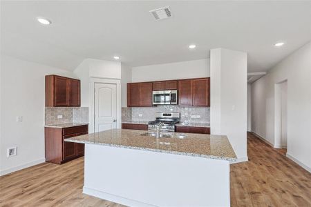 Kitchen featuring a center island with sink, light hardwood / wood-style floors, appliances with stainless steel finishes, and light stone countertops