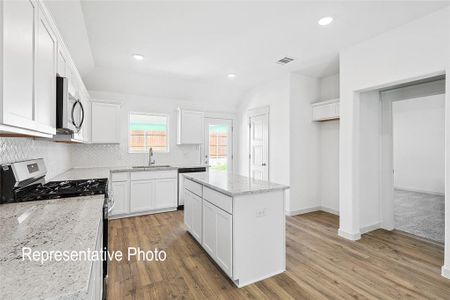 Kitchen with light stone countertops, appliances with stainless steel finishes, a center island, hardwood / wood-style flooring, and white cabinetry