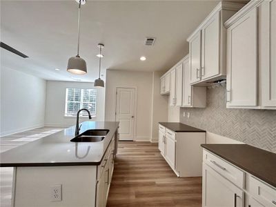 Kitchen with sink, a kitchen island with sink, tasteful backsplash, decorative light fixtures, and hardwood / wood-style floors