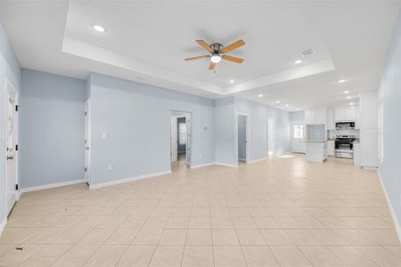 Unfurnished living room with ceiling fan, a raised ceiling, and light tile patterned floors