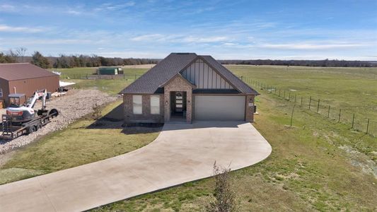 View of front of property featuring concrete driveway, fence, board and batten siding, and a rural view