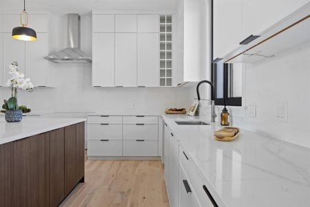 Kitchen with light stone countertops, a sink, white cabinets, wall chimney range hood, and modern cabinets