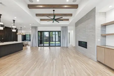 Unfurnished living room featuring beam ceiling, ceiling fan with notable chandelier, tile walls, light hardwood / wood-style floors, and a tile fireplace