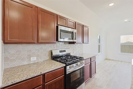 Kitchen with light hardwood / wood-style floors, light stone countertops, appliances with stainless steel finishes, and tasteful backsplash