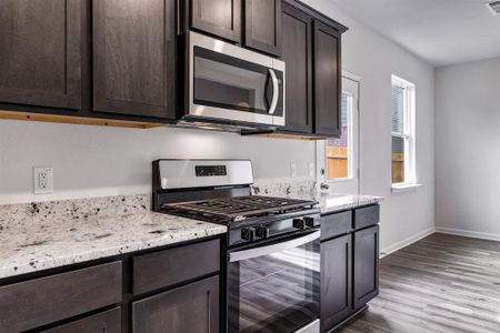 Kitchen featuring dark brown cabinetry, light stone counters, light wood-type flooring, and stainless steel appliances