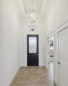 Entrance foyer featuring a raised ceiling, light parquet flooring, and a notable chandelier