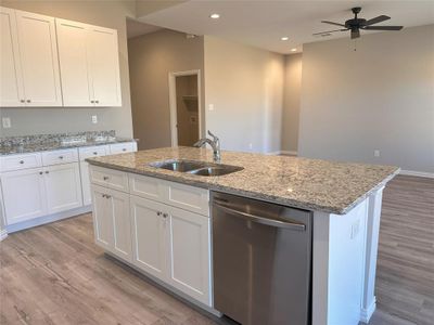 Kitchen with a kitchen island with sink, stainless steel dishwasher, sink, ceiling fan, and white cabinets