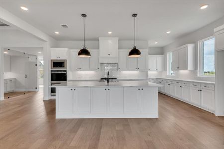 Kitchen with a kitchen island with sink, light wood-type flooring, stainless steel oven, and white cabinetry