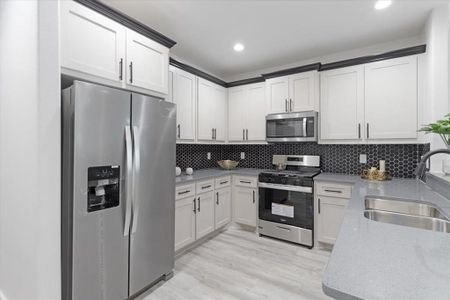 Kitchen featuring light stone countertops, light wood-type flooring, appliances with stainless steel finishes, sink, and tasteful backsplash