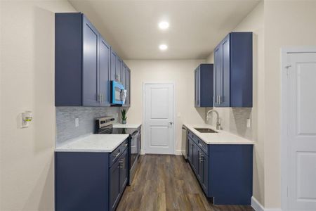 Kitchen featuring appliances with stainless steel finishes, sink, dark hardwood / wood-style flooring, decorative backsplash, and blue cabinetry