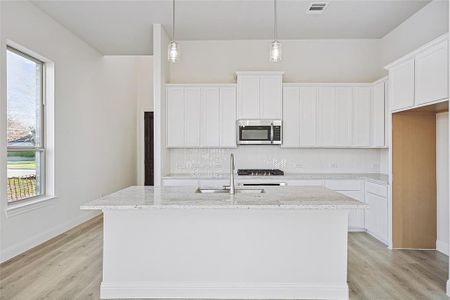 Kitchen featuring white cabinetry, a center island with sink, decorative light fixtures, and sink