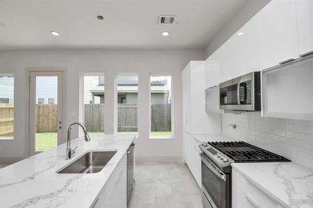 This is a modern kitchen with white cabinetry, quartz countertops, stainless steel appliances including a gas stove, built-in microwave, and ample natural light.