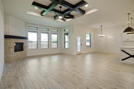 Unfurnished living room featuring coffered ceiling, light hardwood / wood-style floors, a fireplace, ceiling fan with notable chandelier, and beam ceiling