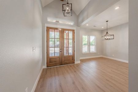 Foyer entrance featuring high vaulted ceiling, light wood-type flooring, french doors, and an inviting chandelier