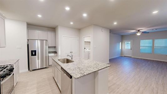 This photo showcases a modern, open-concept kitchen and living area. The kitchen features sleek granite countertops, stainless steel appliances, and ample cabinetry. The living space is bright with recessed lighting, wood-style flooring, and large windows, creating a welcoming atmosphere.