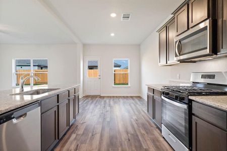 Kitchen featuring appliances with stainless steel finishes, sink, light stone counters, and dark hardwood / wood-style flooring