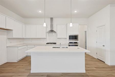 Kitchen with wall chimney exhaust hood, stainless steel appliances, white cabinets, and decorative light fixtures