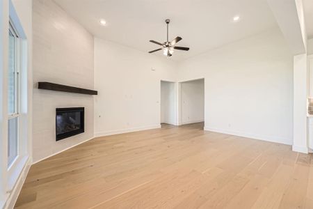 Unfurnished living room with a tile fireplace, light wood-type flooring, plenty of natural light, and ceiling fan