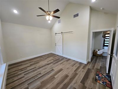 Unfurnished master bedroom featuring luxury vinyl wood-style flooring, a barn door, high vaulted ceiling, designer ceiling fan and back door leading to covered porch and swimming pool.