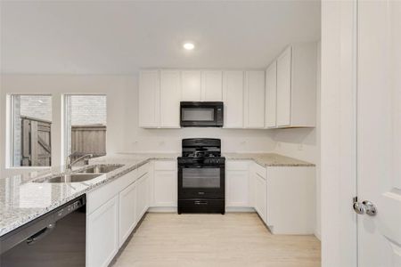 Kitchen with black appliances, sink, white cabinets, light hardwood / wood-style floors, and light stone counters