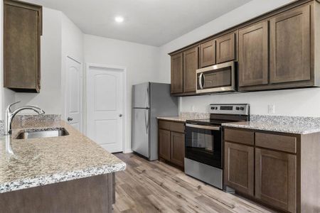 Kitchen featuring sink, dark brown cabinetry, light stone counters, light hardwood / wood-style floors, and stainless steel appliances