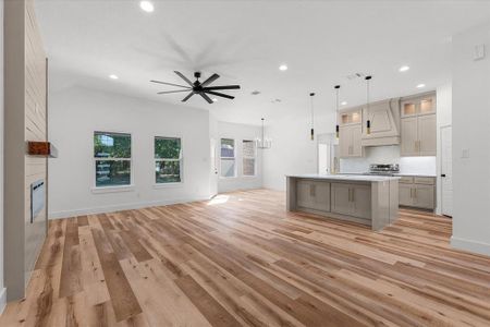 Kitchen featuring premium range hood, an island with sink, light hardwood / wood-style floors, stainless steel stove, and ceiling fan with notable chandelier