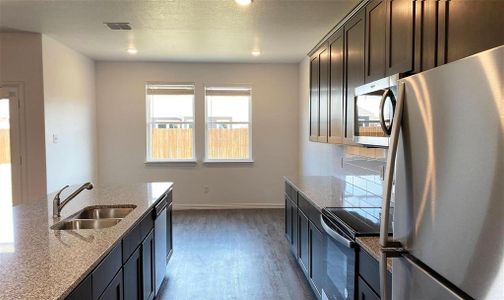 Kitchen with light stone counters, dark brown cabinets, stainless steel appliances, dark wood-type flooring, and sink