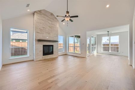 Unfurnished living room featuring light hardwood / wood-style floors, a tiled fireplace, high vaulted ceiling, and ceiling fan