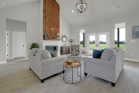 Living room with light wood-type flooring, high vaulted ceiling, a notable chandelier, and french doors