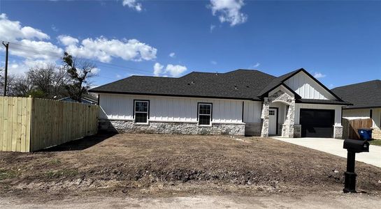 View of front facade featuring stone siding, an attached garage, concrete driveway, and fence