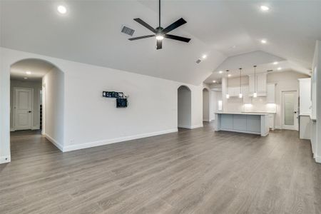 Spacious living room opens to the kitchen with light hardwood / wood-style floors, Plantation shutters, ceiling fan, and lofted ceiling