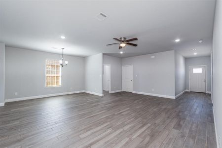 Spare room with ceiling fan with notable chandelier, wood finished floors, visible vents, and baseboards