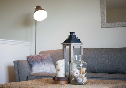 Living room with gray sofa with throw pillow, standing lamp with light on in the corner, and decorative candle and lantern on a wood table