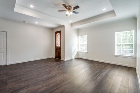 Unfurnished living room featuring crown molding, a tray ceiling, dark wood-type flooring, and ceiling fan