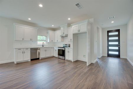 Kitchen with appliances with stainless steel finishes, dark hardwood / wood-style floors, tasteful backsplash, sink, and white cabinets