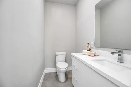 This is a modern, minimalist half-bath featuring a sleek white vanity with an integrated sink and a wall-mounted faucet, complemented by a standard toilet. The neutral gray walls and light flooring give it a clean, contemporary look.